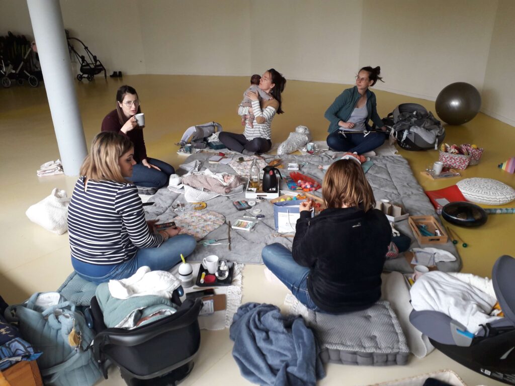 Atelier collectifs avec des mamans qui discutent ensemble et se soutiennent dans leur postpartum, tout en s'occupant de leurs bébés.