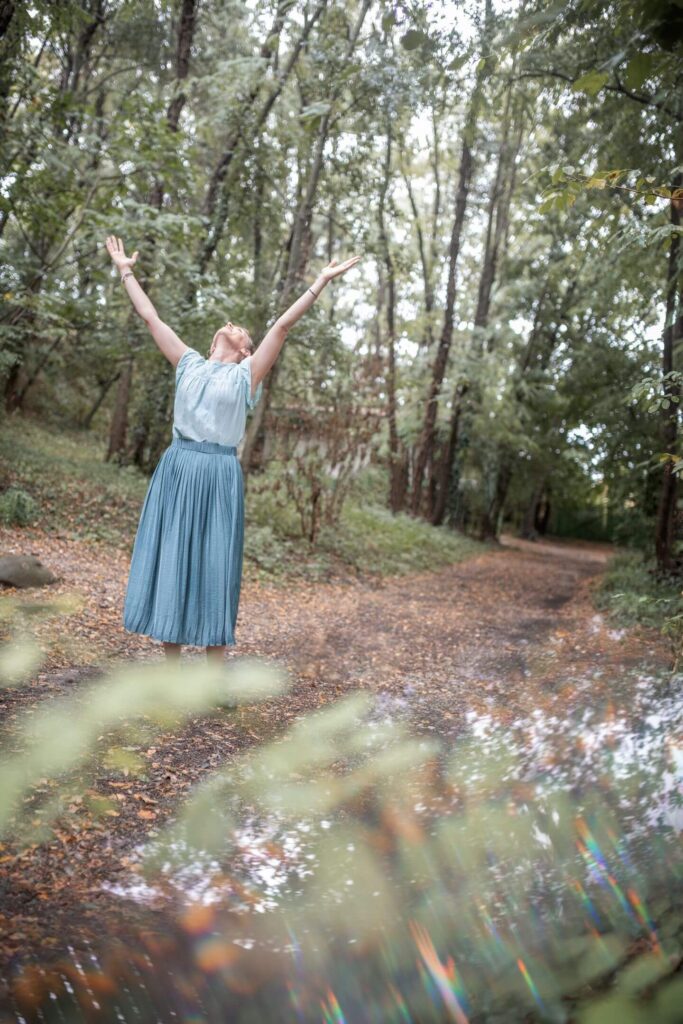 Aurore Mondelin, Doula postnatale à Valence marchant en forêt, les bras levés vers le ciel, symbole d’ancrage, de liberté et d’accompagnement bienveillant des jeunes parents.